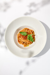 Vegetarian pasta with basil and tomatoes on white plate. Tomato pasta in summer menu with hard shadows Spaghetti with tomatoes on light background. Vegan food - spaghetti marinara
