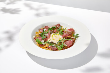 Homemade pasta with pastrami and creamy sauce with cheese. Italian pasta pappardelle with beef and sauce on white table Italian food in summer dining with shadows of sunlight