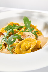 Italian ravioli with meat and mushroom sauce on white plate. Meat tortellini with creamy sauce in summer menu with shadows of tree leaves Ravioli stuffed beef in elegant style