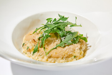 Italian cheese risotto on white plate. Creamy risotto topped parmesan cheese and espuma. Italian risotto with cheese on light background with shadows of leaves Simple italian menu