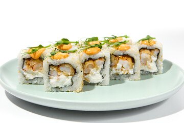 Maki sushi with sesame outside, tempura shrimp inside topped spicy sauce and microgreens. Spicy shrimp maki roll on ceramic plate isolated on white background Sushi roll with crispy prawn on plate