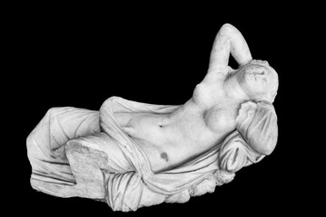 Black and white photo of ancient marble statue in ruins representing a young naked woman resting in...