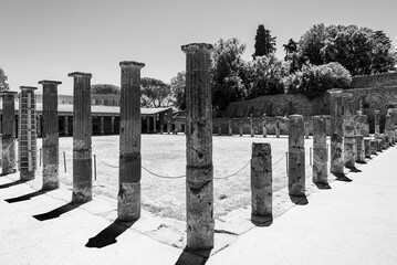 Black and white photo showing ruins of ancient roman columns surrounding a historical site in Pompeii