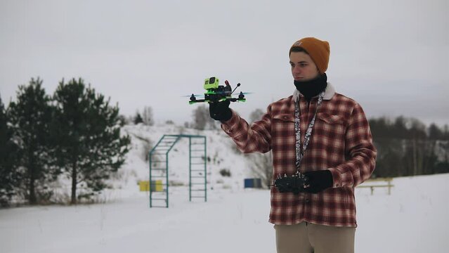 A guy stands in the snow in winter and launches a quadrocopter up. He launches it from his hand