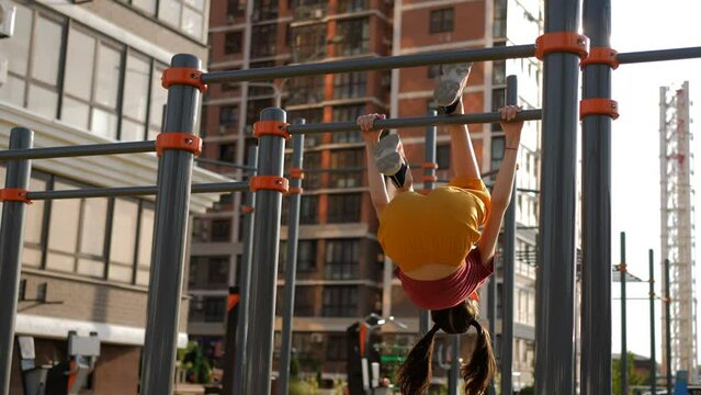 A preteen girl does a somersault on the crossbar. Physical exercises in the yard on horizontal bars.