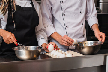 cropped view of chefs holding raw eggs while cooking together in kitchen.