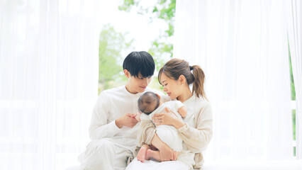 部屋でくつろぐ赤ちゃんを抱いたカップル　家族イメージ