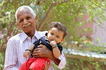 Indian grandfather and Adorable baby outside . Asian old man holding his grandson in his arms . Pali Rajasthan , India