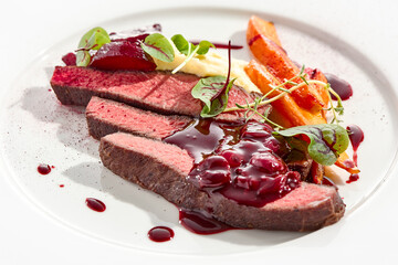 Venison steak with baked vegetables isolated on white plate. Meat steak medium rare roasted with carrot, beetroot and mashed potatoes with cherry sauce. Wild meat in restaurant menu.