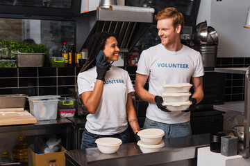 redhead volunteer holding plastic containers and looking at african american woman talking on...