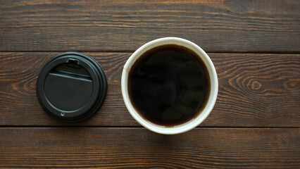 Paper cup with coffee and black plastic lid on dark wooden table top view