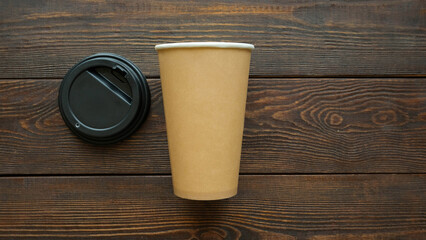 Craft paper cup and black plastic lid on dark wooden table top view