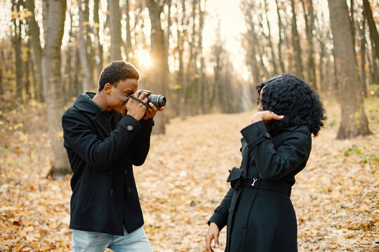 Black man take a photo of black woman in autumn park