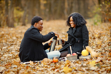 Loving black couple have a picnic in autumn park and drink a tea