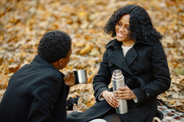 Loving black couple have a picnic in autumn park and drink a tea