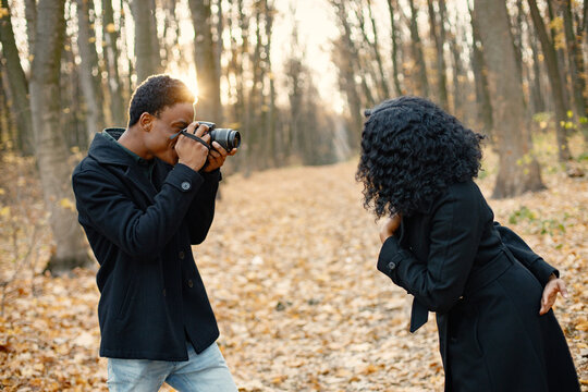 Black man take a photo of black woman in autumn park