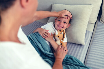 Shot of worried mother taking temperature of her little son who is lying on the sofa with fever. Mother hand taking the temperature of her boy on a couch in the living room at home.