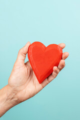 Fototapeta na wymiar Woman hand holding red wooden heart on light blue background. Love, care, donation concept