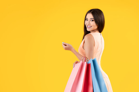 Pretty asian woman holding shopping bags on a yellow background, looking at camera, half length. Summer sales concepts.