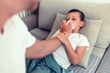 Shot of a young father looking after his sick son at home. Adorable son with a runny nose and resting in the living room.