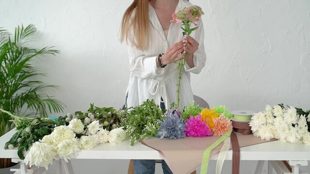 Florist at work: a pretty young brown-haired woman with long hair in a shirt makes a trendy modern bouquet of different flowers. Multi-colored flowers are the result of dyeing fresh flowers through
