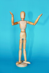 yellow wooden mannequin poses and gestures with his hands on a blue background