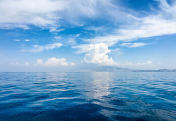 A background of a calm ocean with blue sky and white clouds and reflections in the water