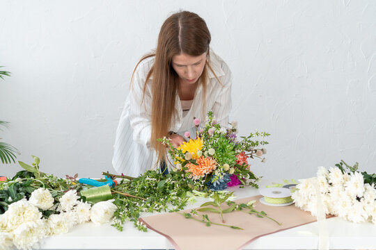 Portrait of a girl florist with long hair presents a bouquet of chrysanthemums. Florist at work. Education, master class, floristry courses