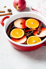 Mulled wine with orange, apple and spices in red saucepan, gray background. Autumn or winter cozy drink.