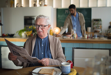 Elderly man enjoying breakfast and reading newspaper in nursing home care center.