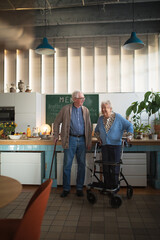 Senior man and woman walking with walker indoors in retirement nursing hme.