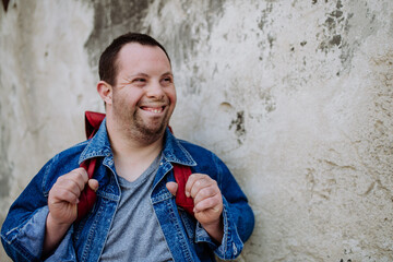 Portrait of happy young man with Down sydrome with backpack in street, smiling.