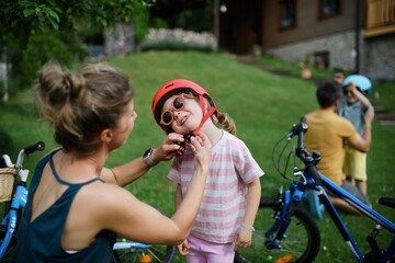 Young mother with little daughter preaparing for bike ride, putting on helmets.