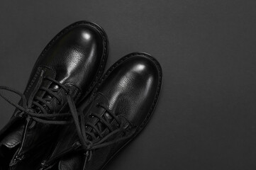 Classic autumn shoes. Fashionable youth black leather boots on black background flat lay top view....