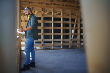 Handyman chcecking blueprints and working on wooden construction site, diy eco-friendly homes concept.