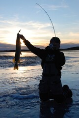 An ice angler with a pike at sunset 