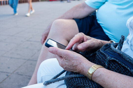 detalle de mujer mayor con movil en la calle, al lado su pareja en pantal&oacute;n corto y sobrepeso. Concepto de vida sedentaria, tecnolog&iacute;a, m&oacute;vil personas de la tercera edad