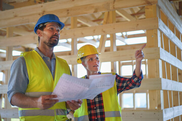 Construction engineers or architects with blueprints checking eco building site of wood frame house
