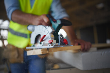 Close-up of construction worker working with eletric saw inside wooden construction of house, diy...