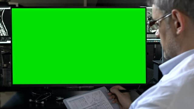 Doctor Holding A Clipboard And Looking At Green Screen Monitor