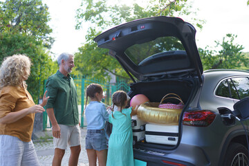 Family with little children loading car and waiting for charging car before going on holiday.