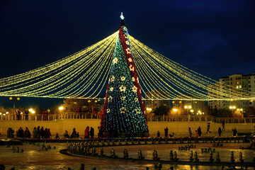 Long exposure night shot of a uniquely decorated main Christmas tree in the square after rain with reflection.
