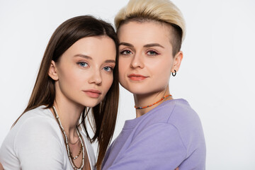 young lesbian girlfriends with makeup looking at camera isolated on grey.