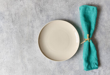 Empty plate and linen rolled up tied napkin on gray concrete background in close-up