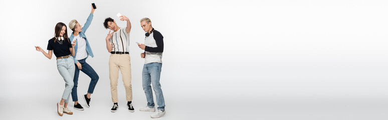 Obraz premium happy friends taking selfie on mobile phones and dancing on grey background, banner.