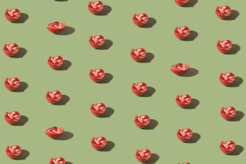 Creative pattern made of half fresh pomegranates on green background with shadows. Refreshment...
