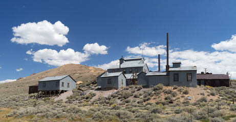 Standard Mill buildings in the ghost town of Bodie shown against a blue sky and beautiful clouds. Bodie is a registered California Historical Landmark