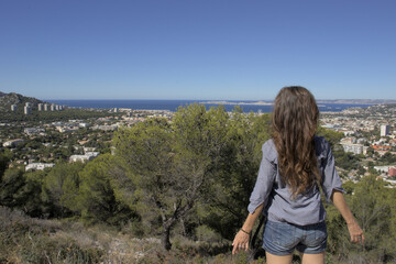 Naklejka premium A woman stands in front of a landscape of city, nature and sea.