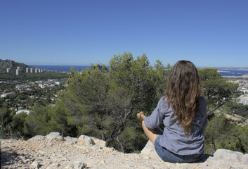A woman sits cross-legged above a landscape of nature, city and sea.