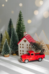 Miniature house and fir trees with red car with Christmas Tree on white background. Winter cute landscape. Cozy small world. Christmas decorations, holiday concept.